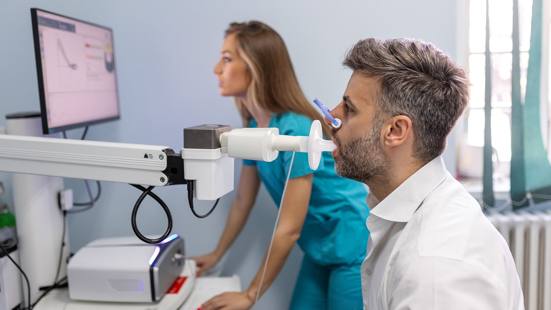 A man and a woman are operating medical equipment, possibly conducting a medical procedure or examination, with screens displaying various data points and images.