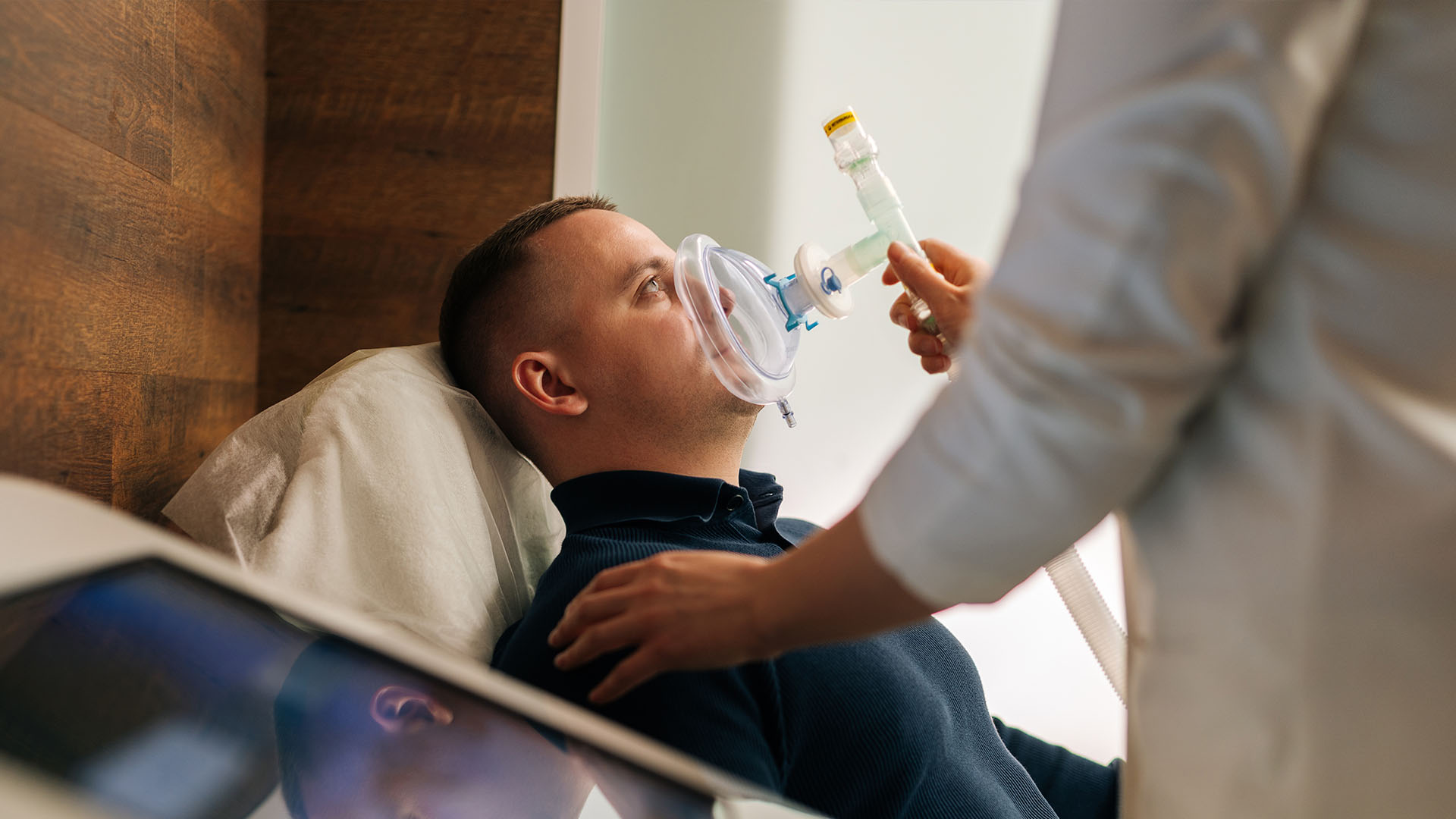 A man lying on a hospital bed receiving oxygen from a medical professional.
